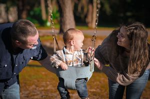 A person swings on a playground swing set with autumn trees in the background during a sunny day.