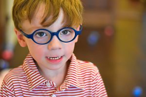 A child wearing blue glasses and a red striped shirt smiles warmly at the camera.