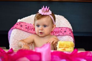 A baby in pink attire sits surrounded by donuts and colorful decorations during a festive photoshoot.