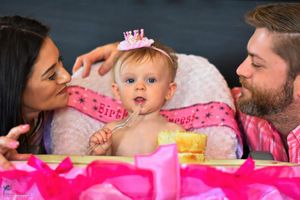 Baby in pink dress and crown celebrates first birthday with cake smash photo session.