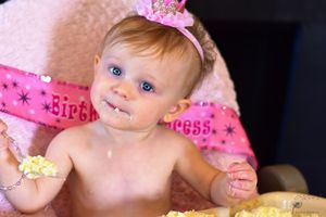 Close-up of baby wearing pink crown during first birthday cake smash celebration.
