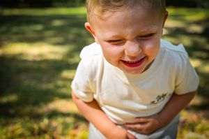 A child wearing a white shirt plays outdoors in dappled sunlight on a warm summer day.