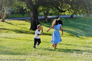 Children run and play together on a sunny grassy hill in a park setting.