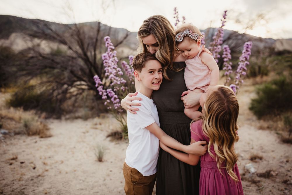 Intimate family moment captured in desert setting with pink and purple desert flowers.