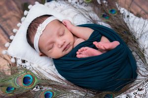 Sleeping newborn baby wrapped in teal fabric with peacock feather styling during studio newborn photoshoot in Hyderabad