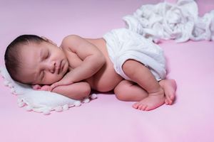 Sleeping newborn baby posed on soft pink background during professional studio newborn photoshoot in Hyderabad