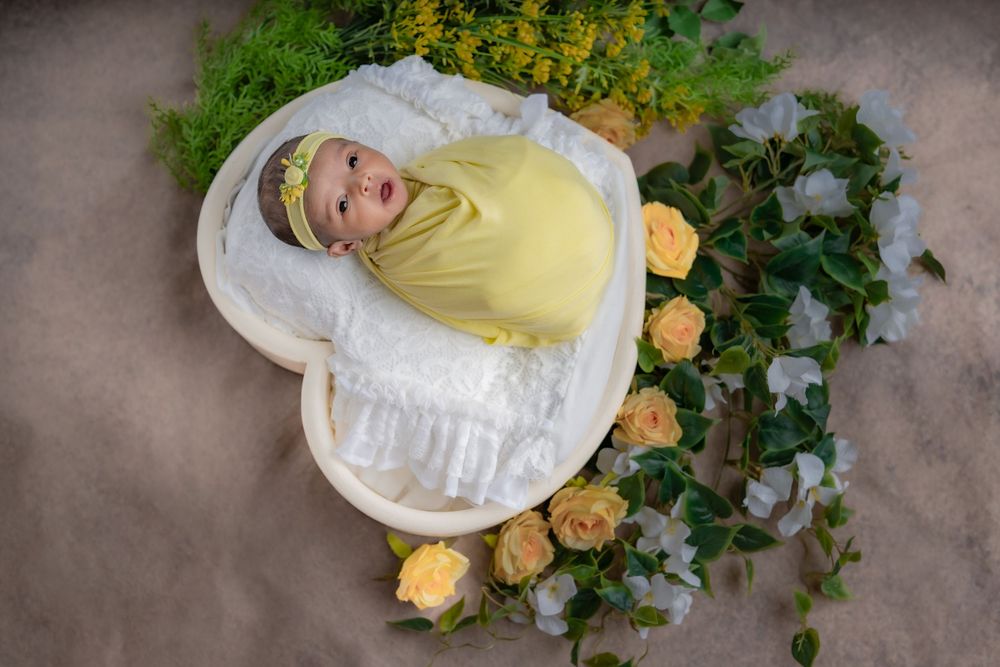Sleeping newborn baby wrapped in yellow, placed in floral setup during studio newborn photoshoot in Hyderabad