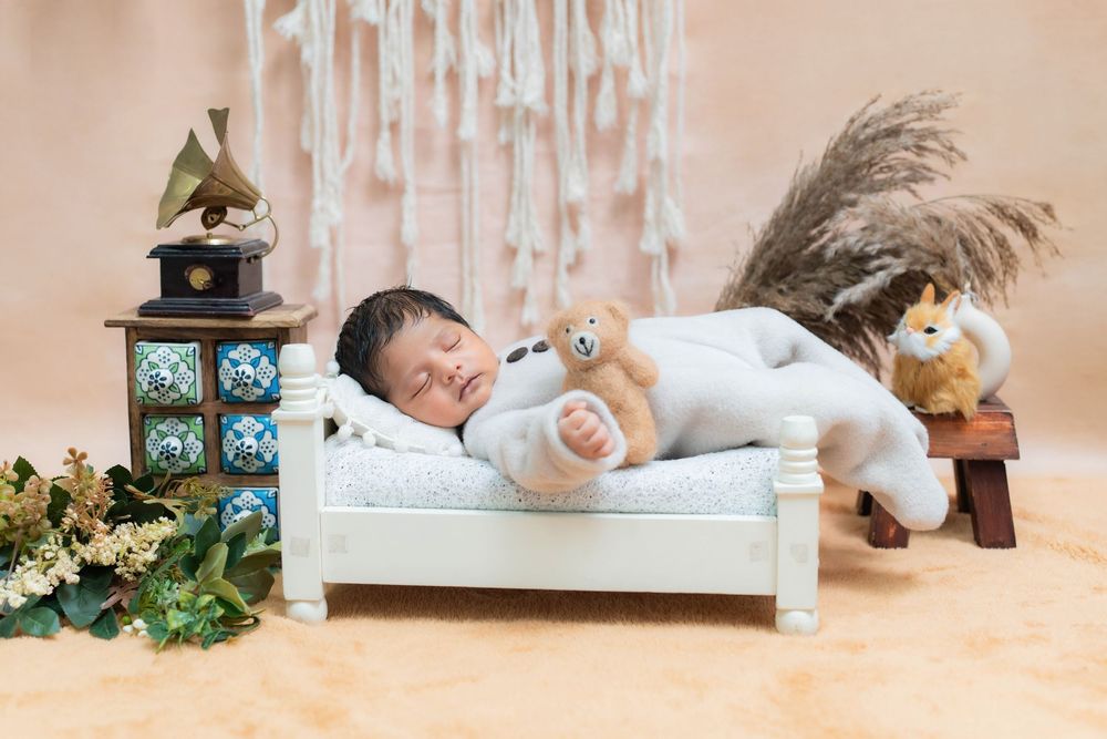 Sleeping newborn baby on white bed with soft props during studio newborn photoshoot in Hyderabad