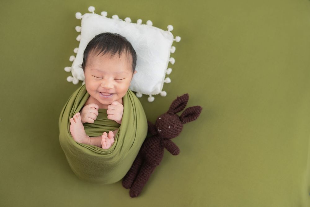 Sleeping newborn baby wrapped in green fabric, featured in home page cover for newborn photography studio in Hyderabad