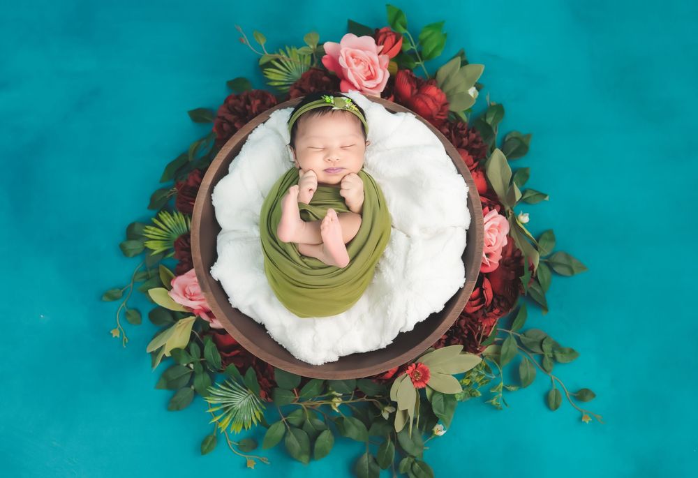 Sleeping newborn baby wrapped in green, placed in floral bowl setup during studio newborn photoshoot in Hyderabad