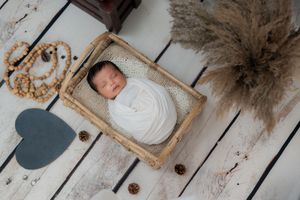Newborn baby wrapped in white, sleeping in wooden basket during studio newborn photoshoot in Hyderabad.
