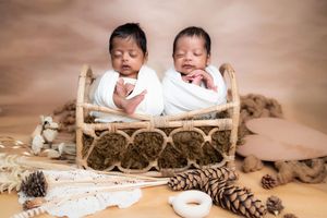 Twin newborn babies wrapped in white, seated in wooden basket during studio newborn photoshoot in Hyderabad