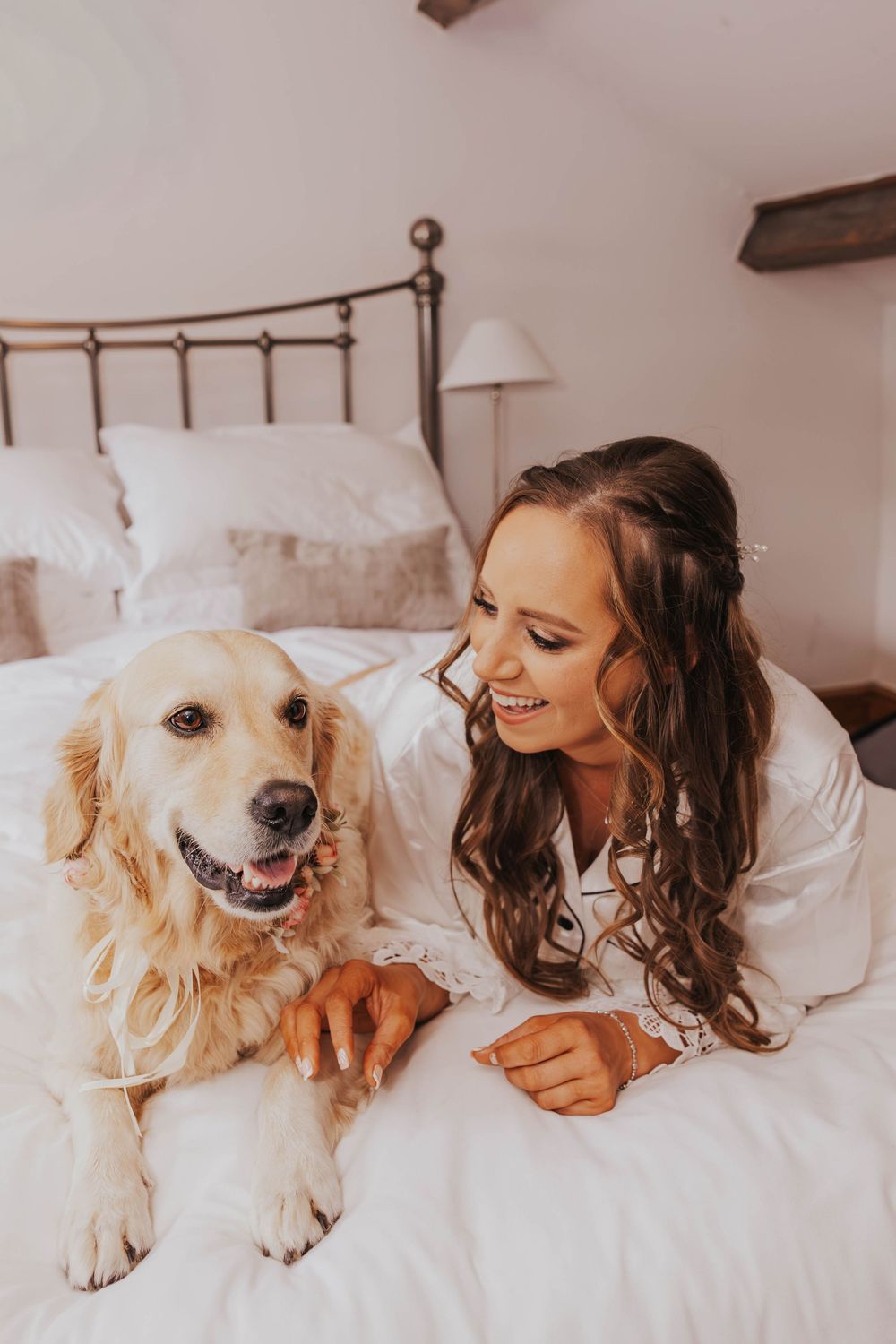 A golden retriever and person share sweet moments together while relaxing on a white bed in a cozy bedroom setting.