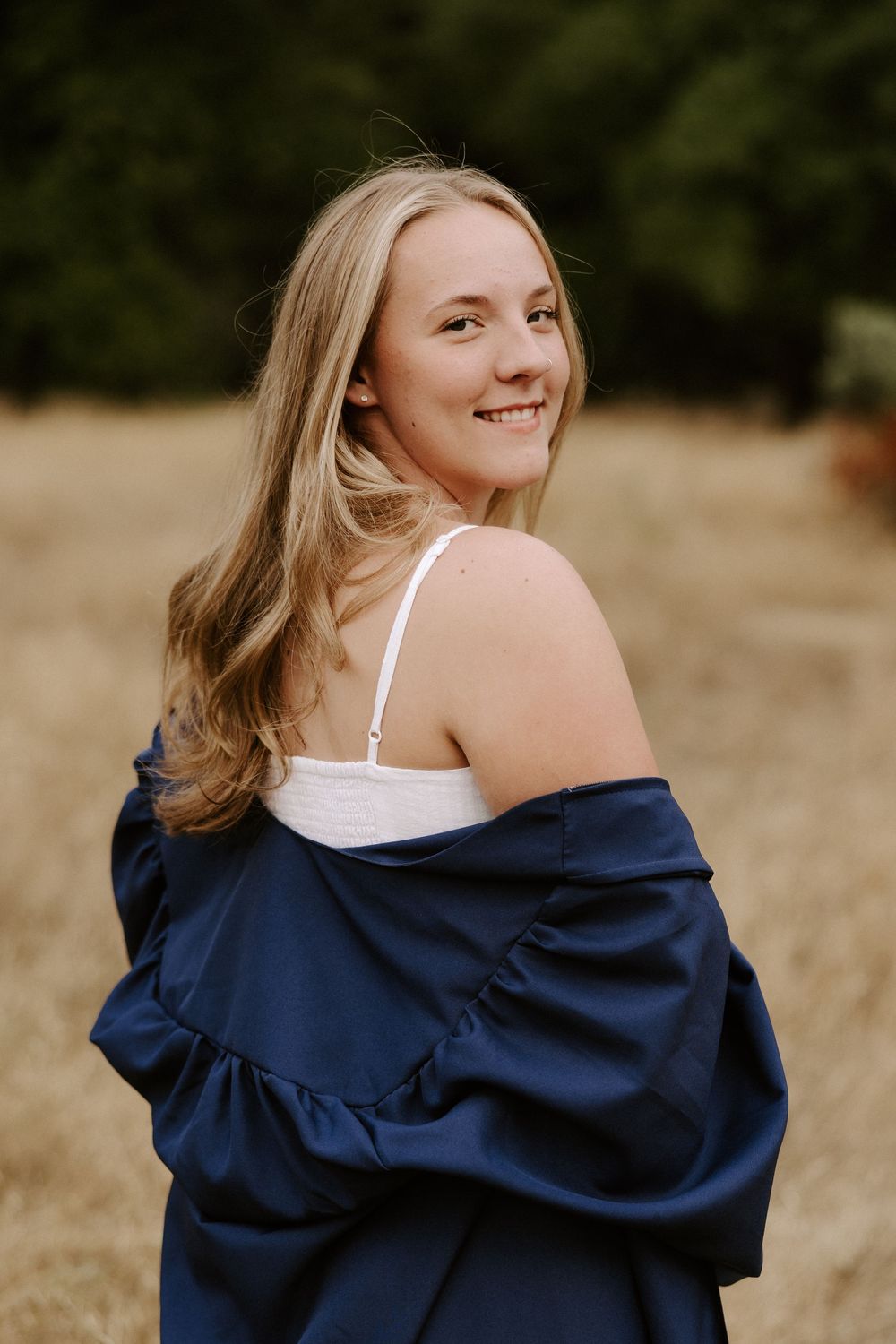 A navy graduation gown is styled with a white dress in an artistic outdoor portrait series.