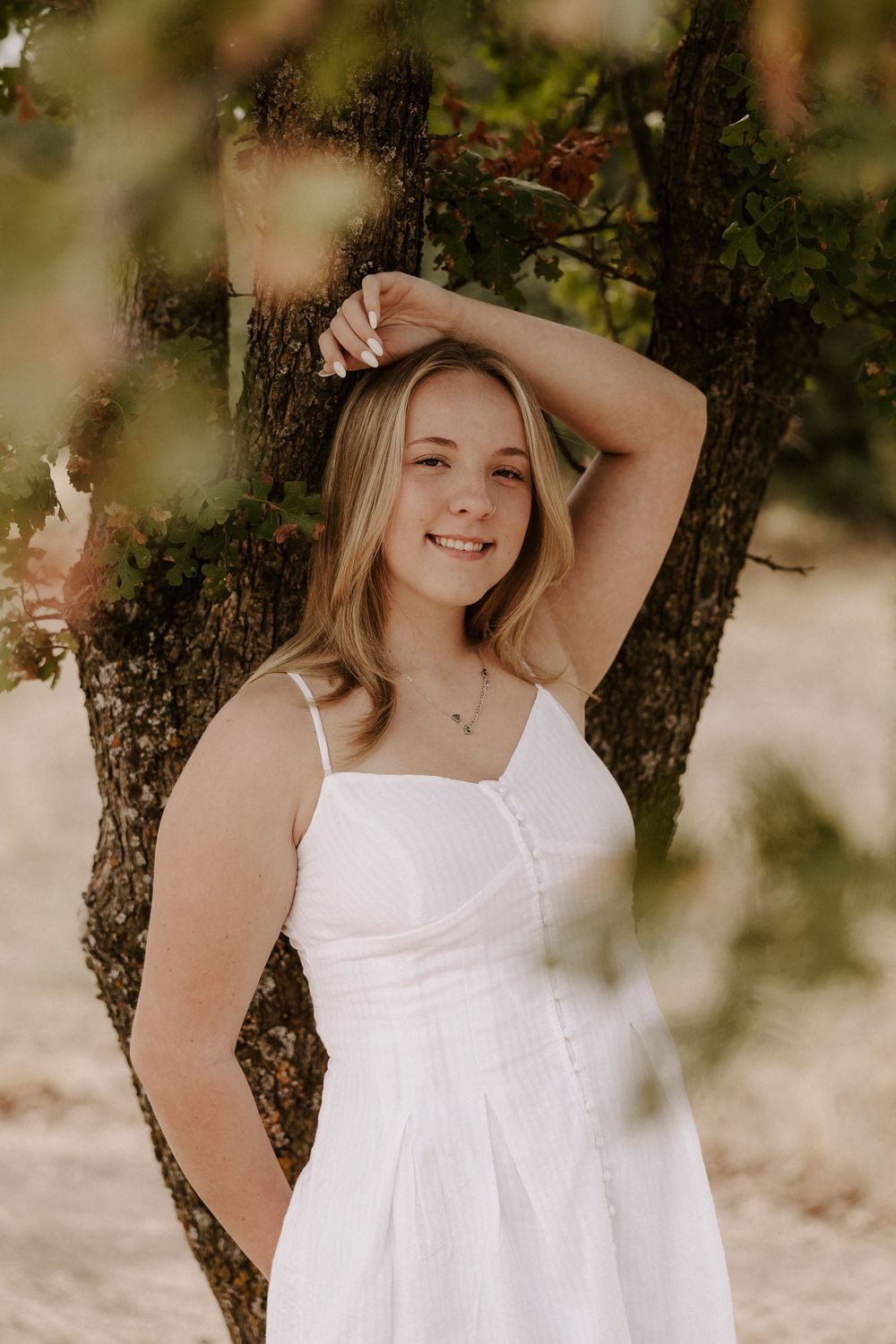 A summer portrait in a white sundress posed against a tree with soft natural lighting.