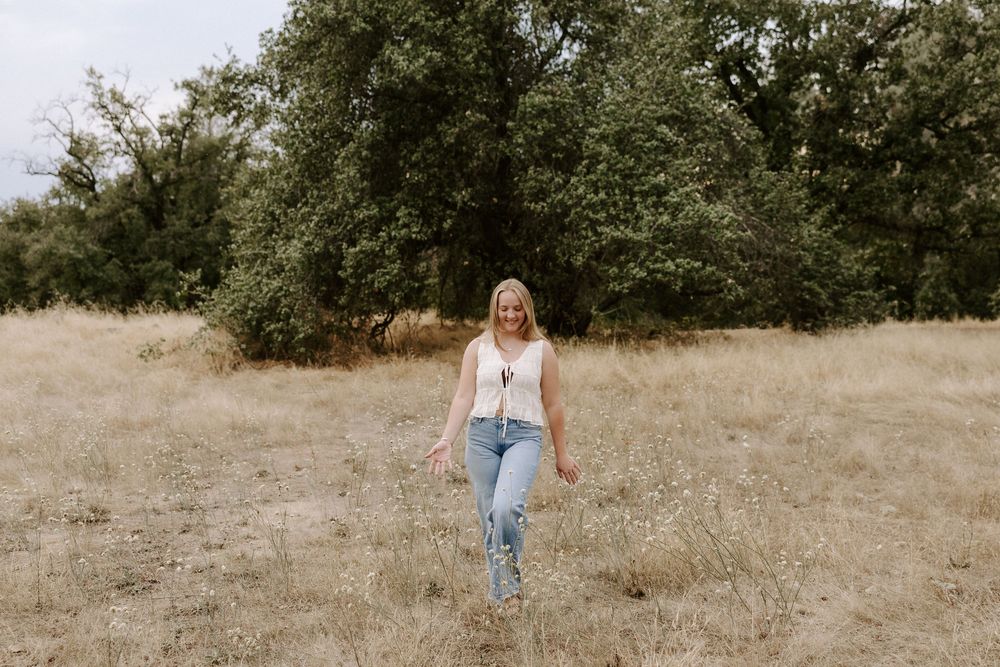 Someone walks through a dried grass field wearing casual attire and light colored clothing.