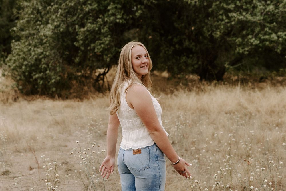 A person wearing jeans and a white top poses playfully in a golden field during sunset.