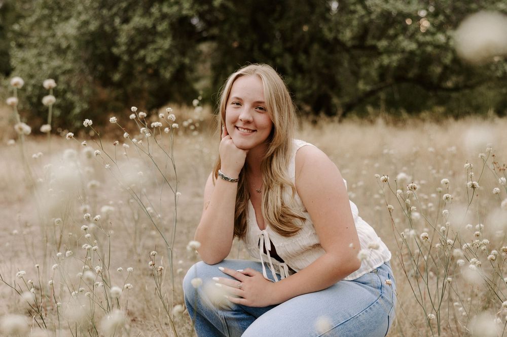 A person sits in a field of white wildflowers during a golden hour photoshoot.