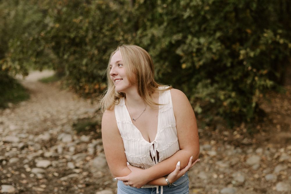 A person poses in a white top and jeans among wildflowers during a summer outdoor portrait session.