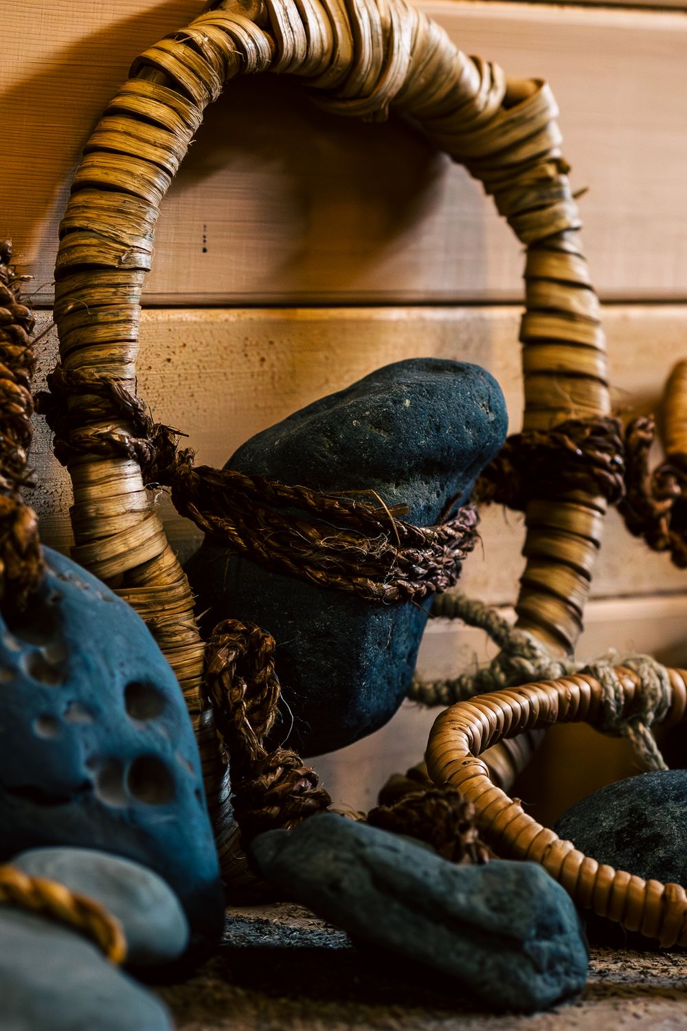 A series of artistic photographs showing a dark blue skull sculpture with woven natural fiber rings in a dramatic lighting.