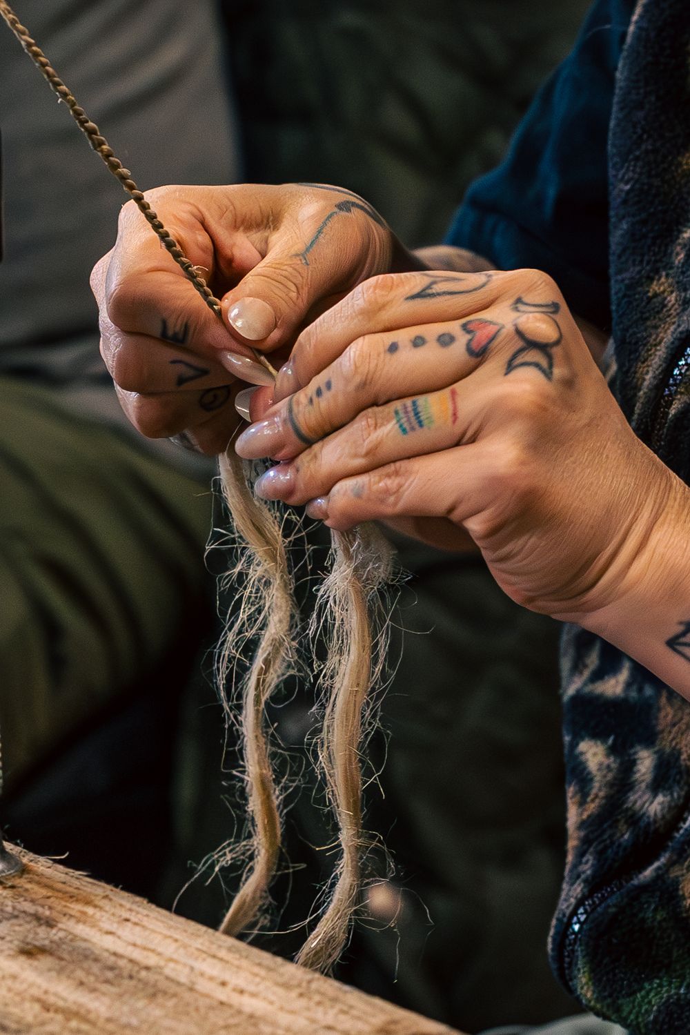 Close-up of hands with tattoos working with natural jute or hemp fibers on a wooden surface.