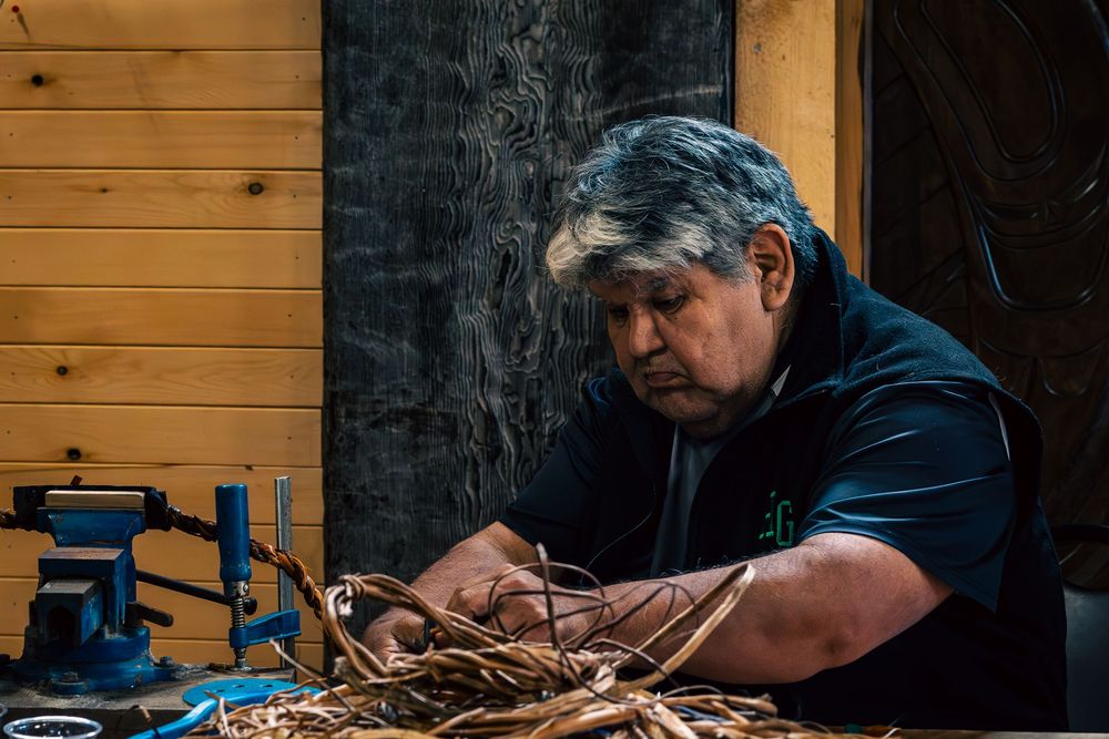 Traditional craftsperson working intently with rope materials at a wooden workbench with a blue vise.