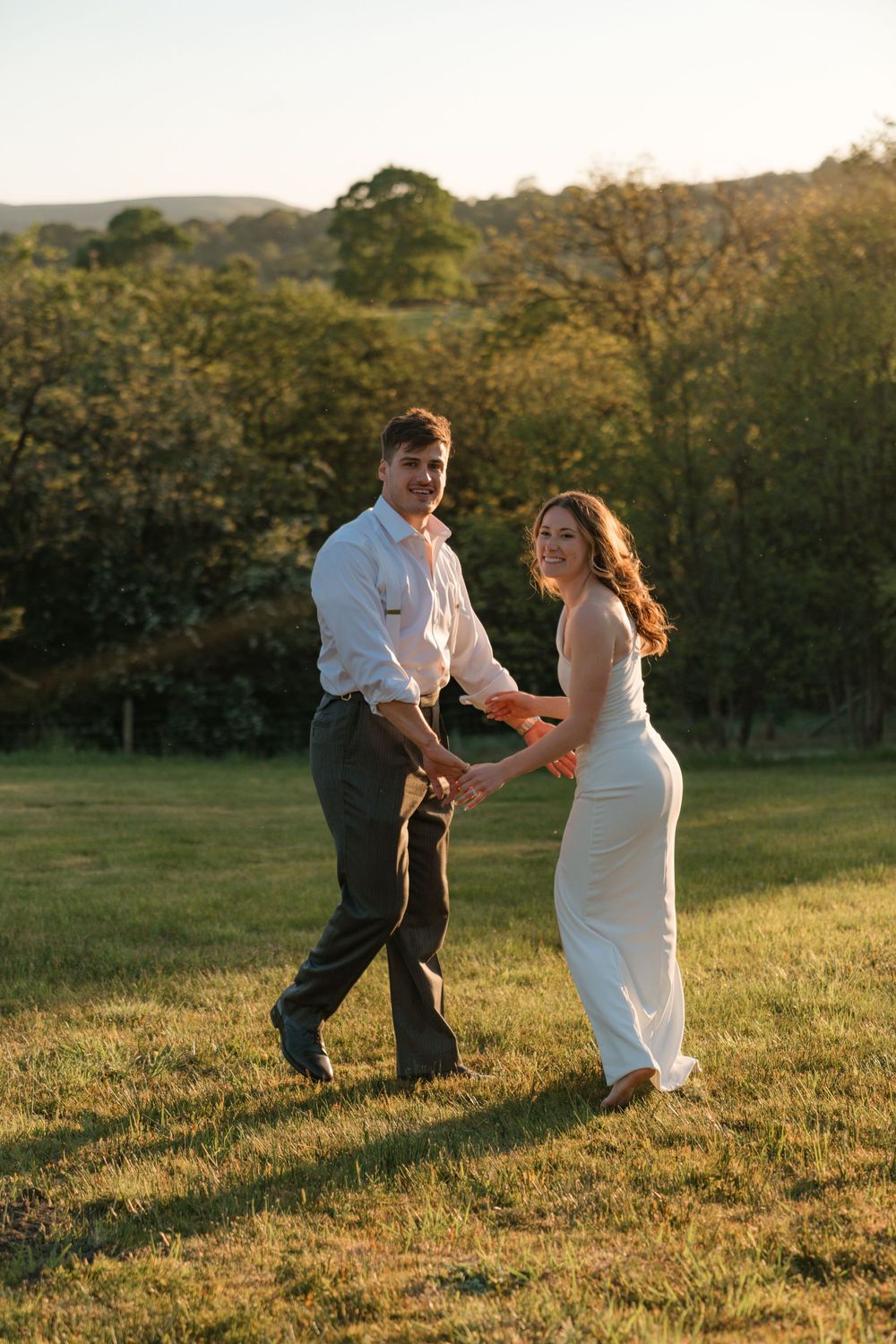 A couple dances together in a grassy field at golden hour, creating a romantic silhouette against the sunset.