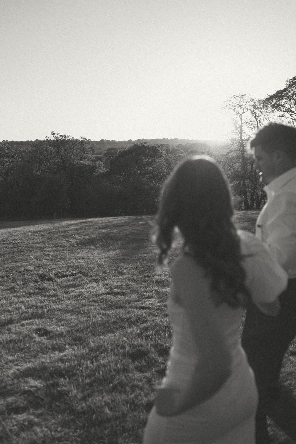A couple embraces in silhouette against a sunlit meadow during golden hour.