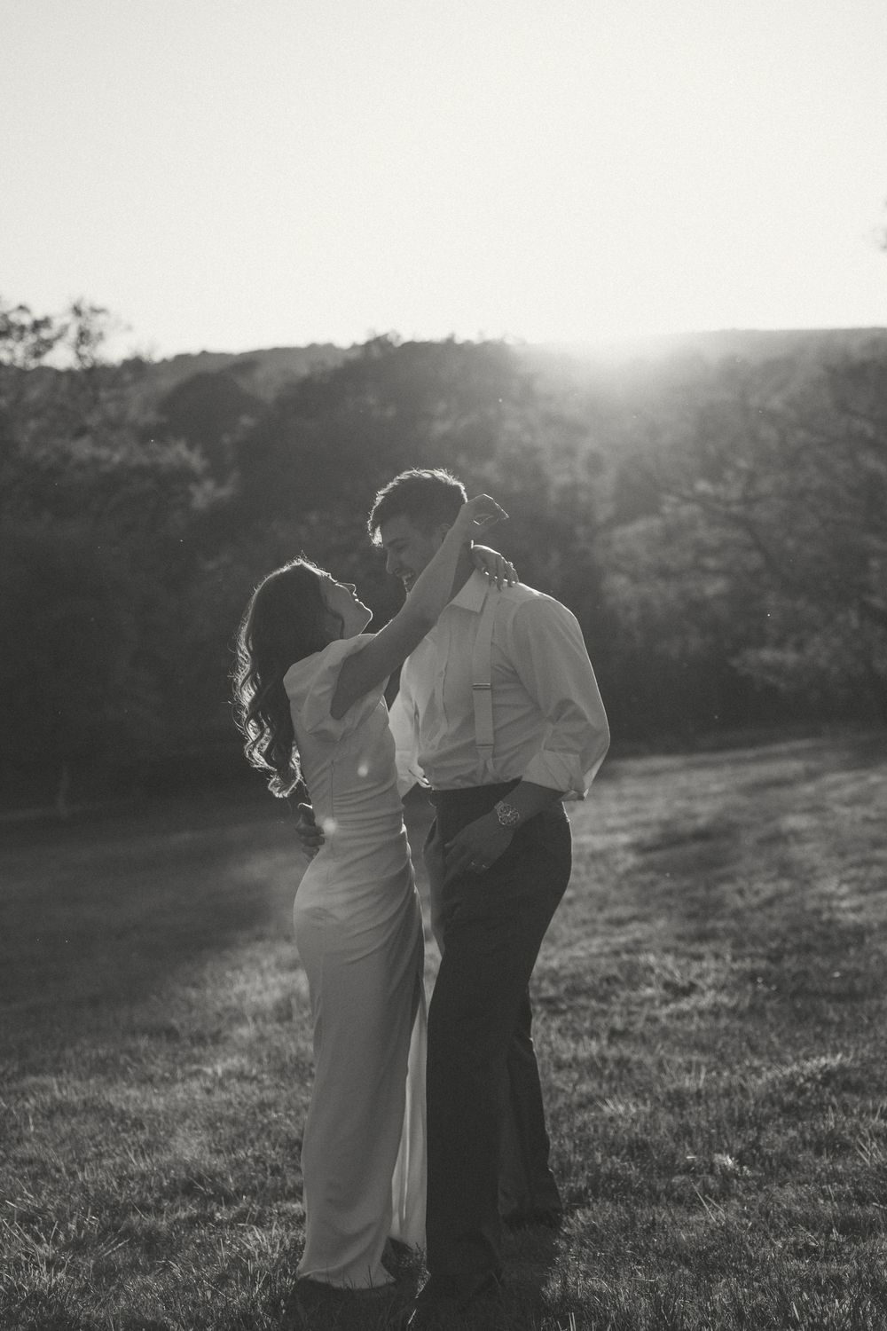 A romantic black and white silhouette of a couple embracing in a sunlit field at golden hour.