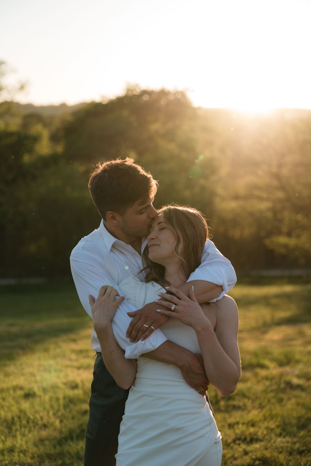 A couple shares a romantic embrace in a sunlit meadow during golden hour.