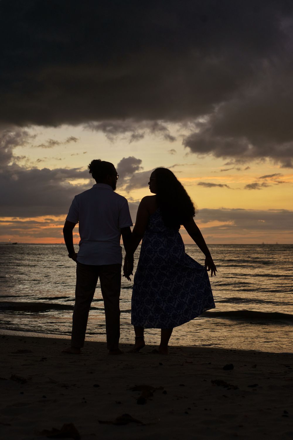 Silhouettes of people exploring a beach at sunset with dramatic cloudy skies over the ocean.