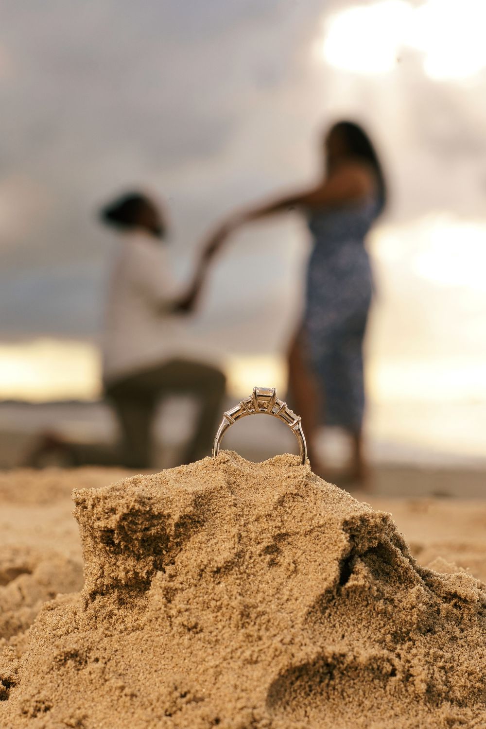 A close-up sequence showing a sandcastle being built on a beach with blurred figures in the background at sunset.