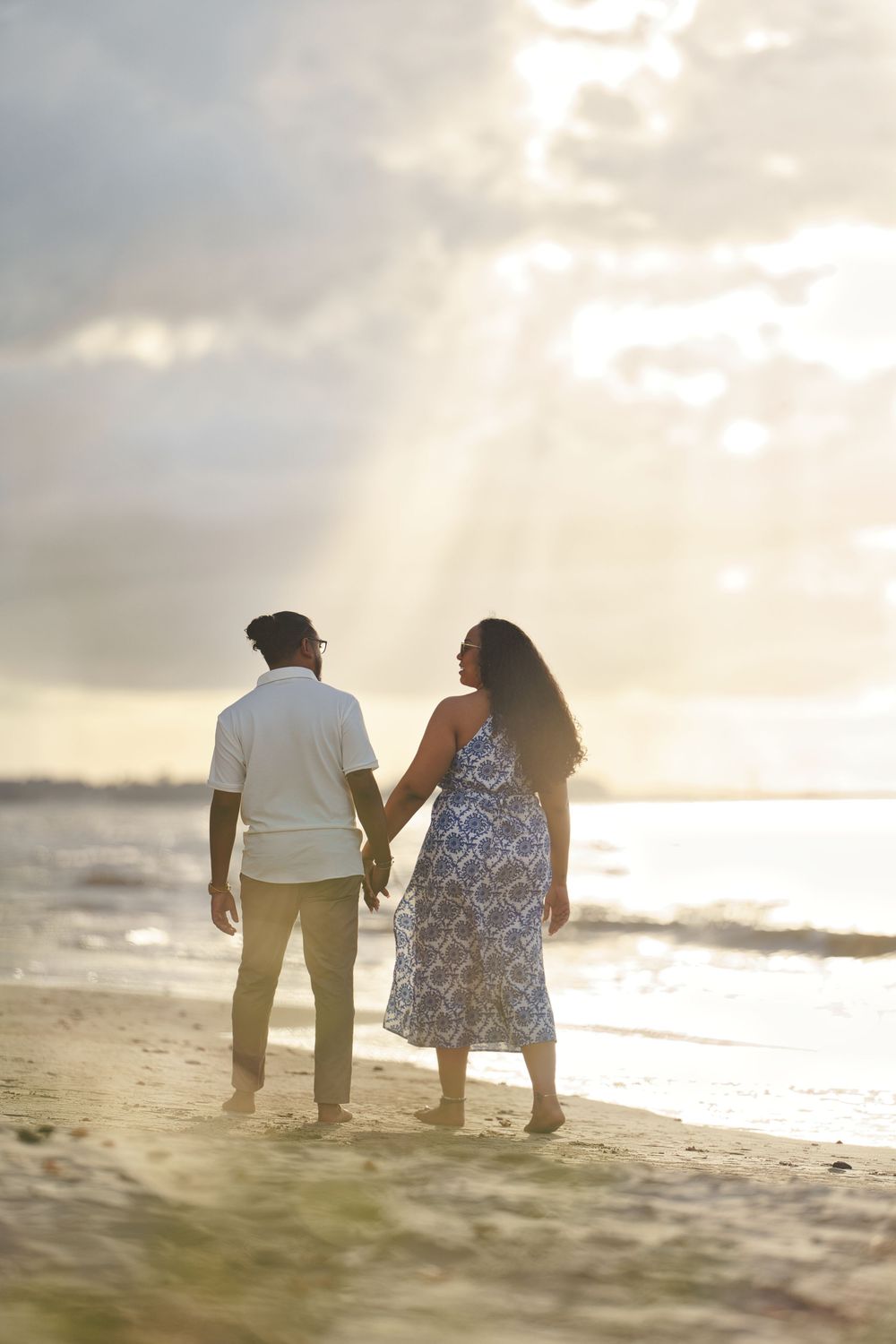 A couple walks hand in hand along a serene beach at sunset, creating romantic silhouettes against the golden sky.