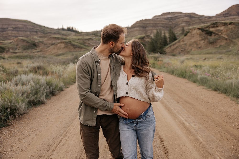 A couple shares intimate moments on a scenic dirt road surrounded by desert mountains and sagebrush landscape.
