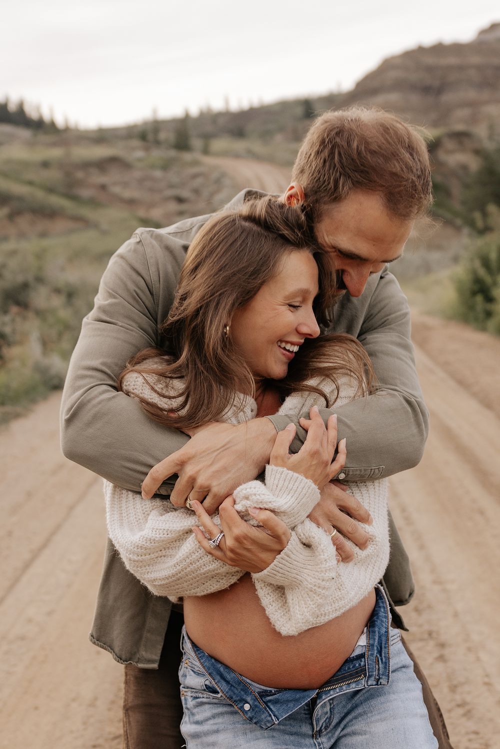 A maternity couple embraces on a dirt road in the calgary alberta during a photo shoot.