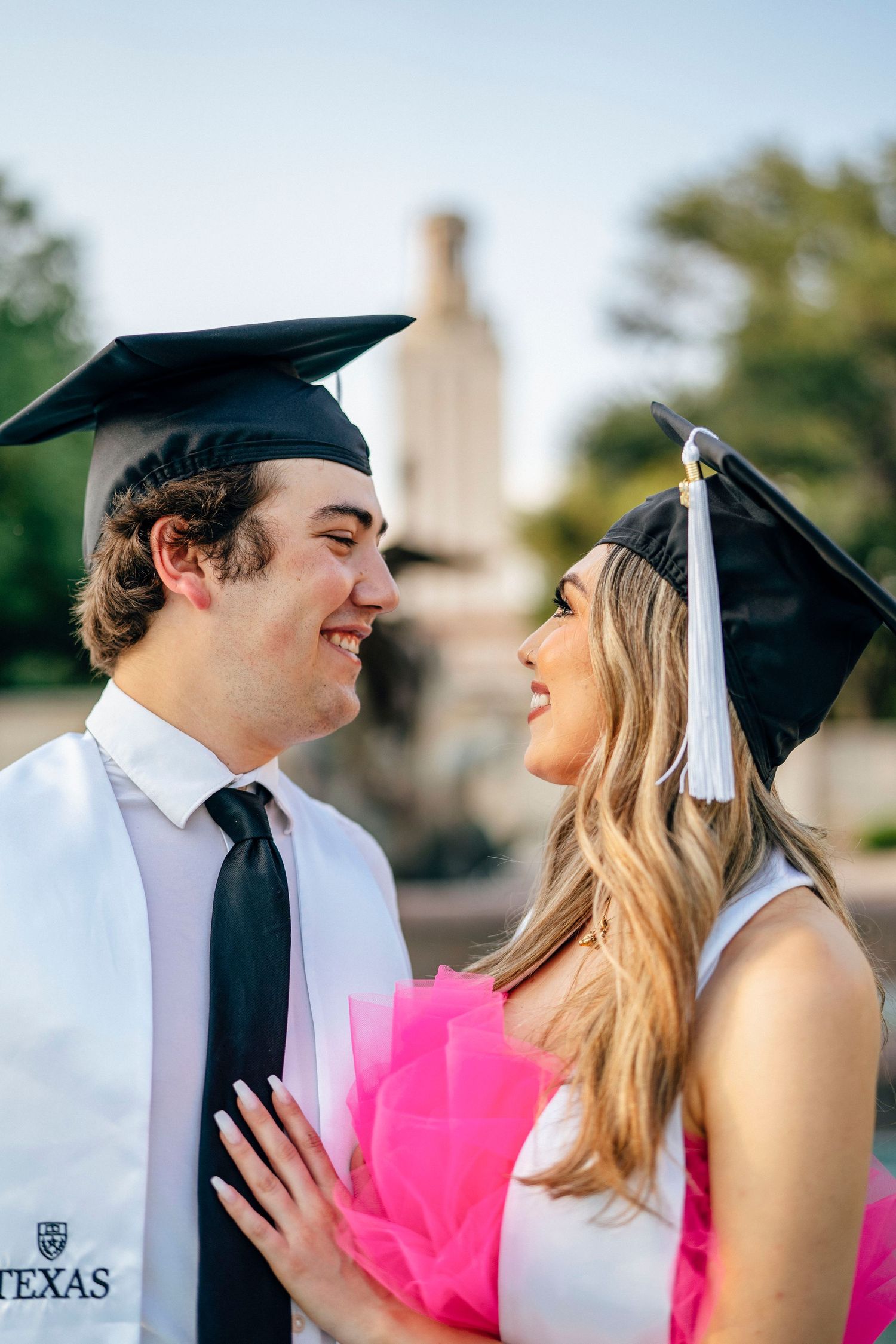 A graduation photo session showing two graduates in caps and gowns sharing a joyful moment together outdoors.