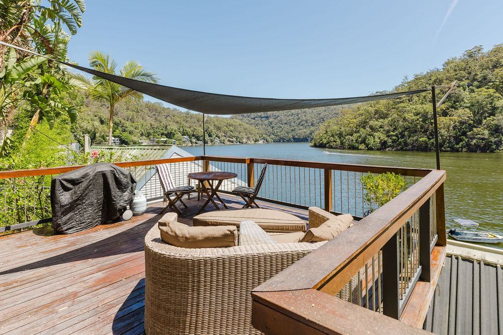 Waterfront deck with wicker furniture and sail shades offering panoramic views of a serene lake surrounded by trees.