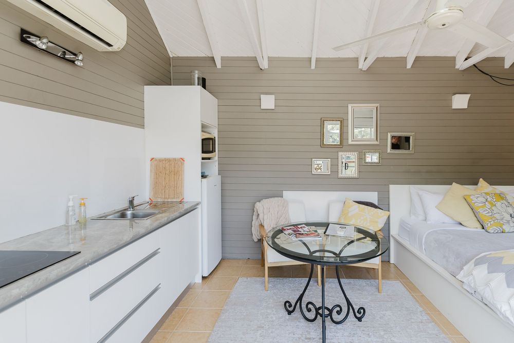 Modern studio apartment interior with white kitchen cabinets, round metal table and daybed against gray walls.
