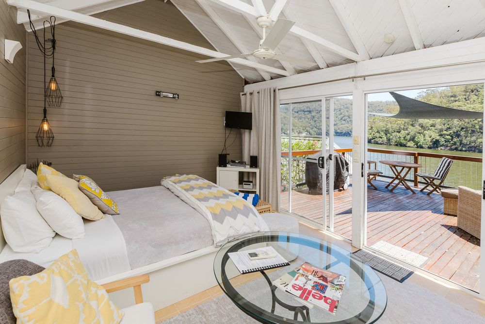 Modern bedroom with sliding glass doors opening to a balcony deck, featuring white bedding and yellow accent pillows.