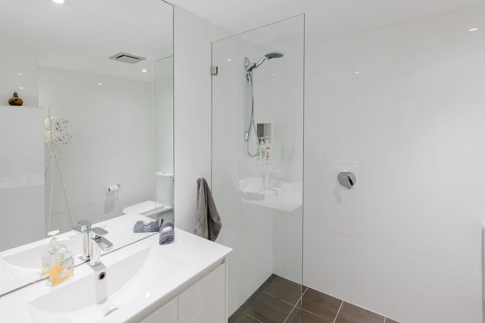 Modern white bathroom interior with glass shower enclosure, pedestal sink, and chrome fixtures against bright walls.