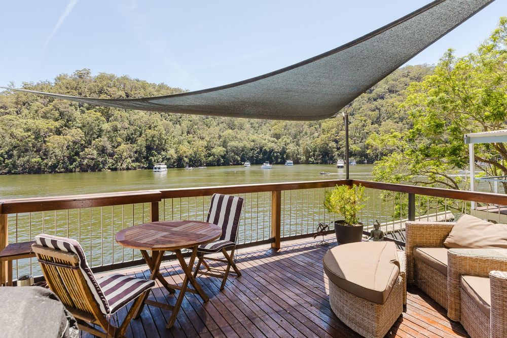 Scenic lakeside deck with outdoor seating and shade sails overlooking tranquil water and wooded shoreline.