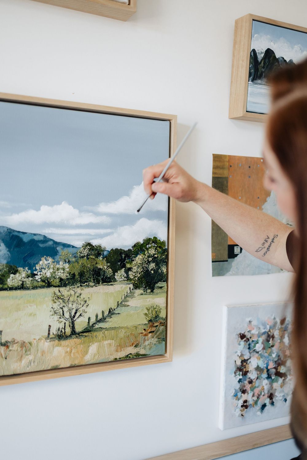 Gallery wall displays landscape paintings and artwork in wooden frames against white walls.