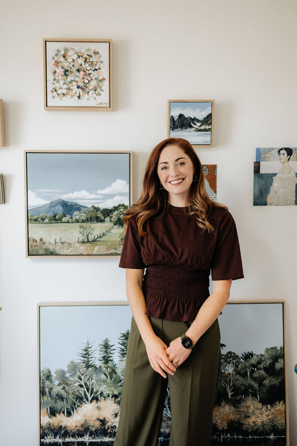 An art studio space with multiple framed landscape paintings displayed on a bright white wall.