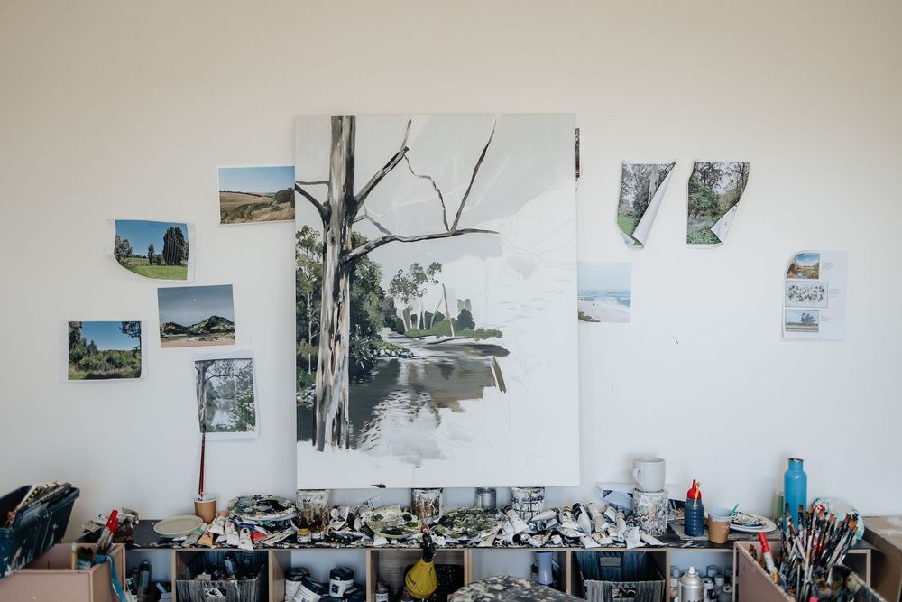 A gallery wall displays black and white landscape photographs alongside sketches in a minimalist white room setting.