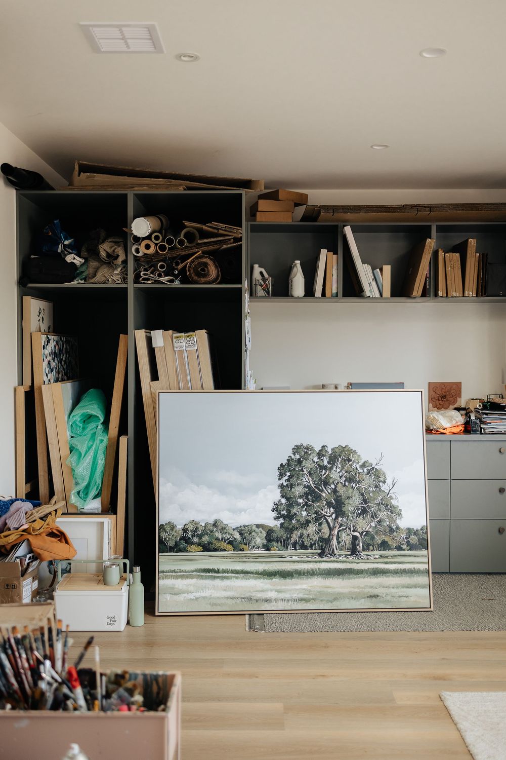 A panoramic series of four connected photos showing a landscape painting being displayed on a wooden shelf with books.