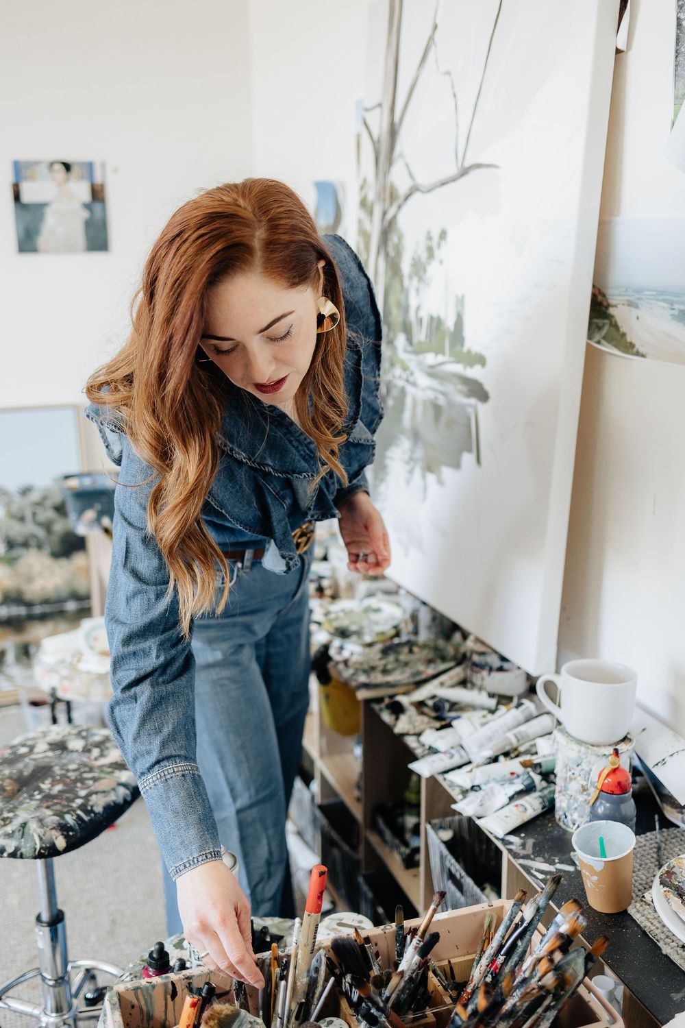 Artist working at a studio desk with various painting supplies and tools.