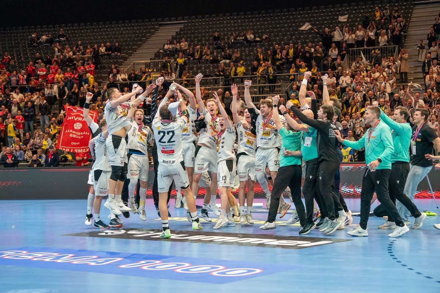Handball players and team members celebrate together on the court after an exciting match victory.