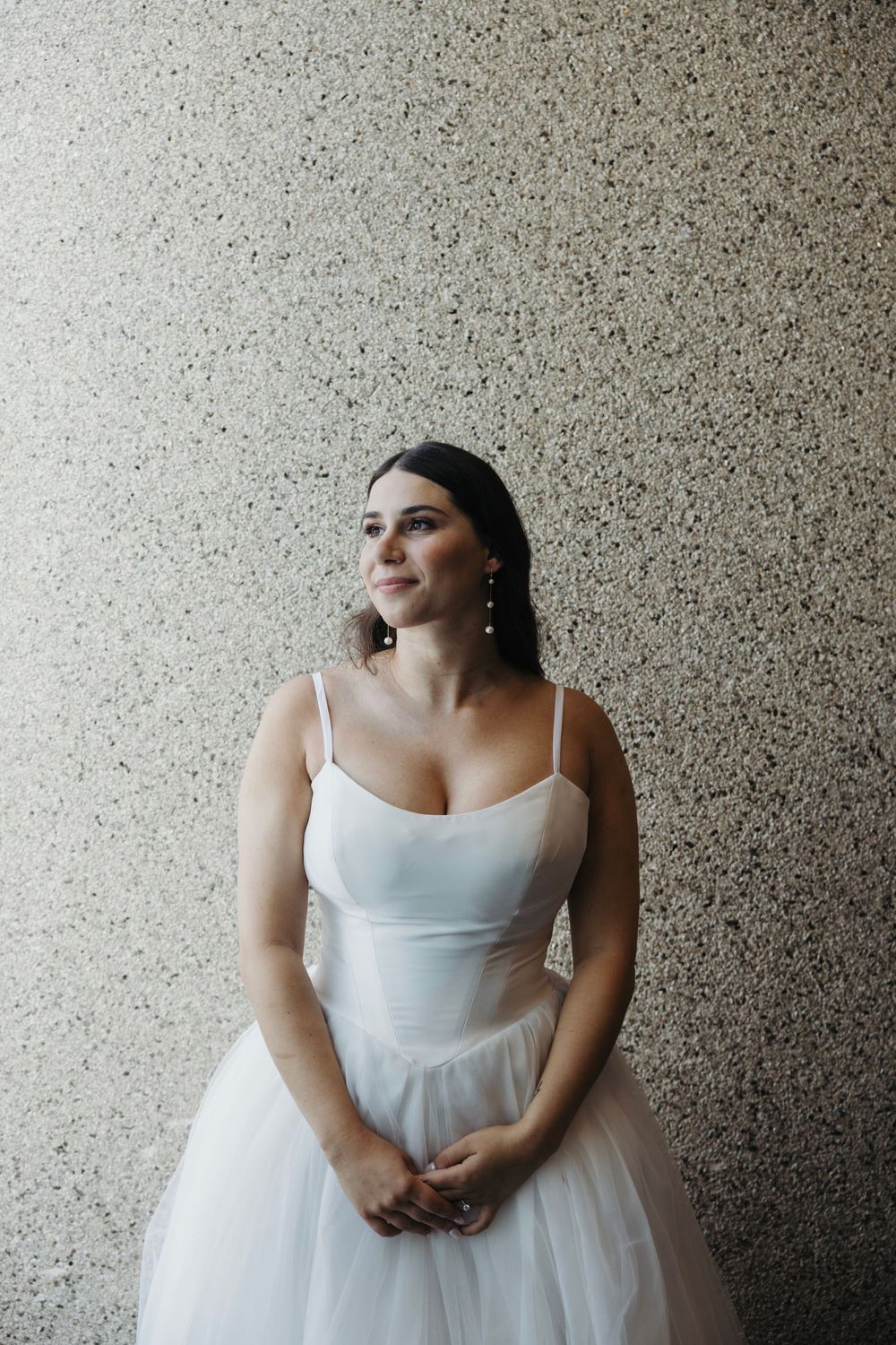 White wedding gown against a textured grey wall in natural lighting.