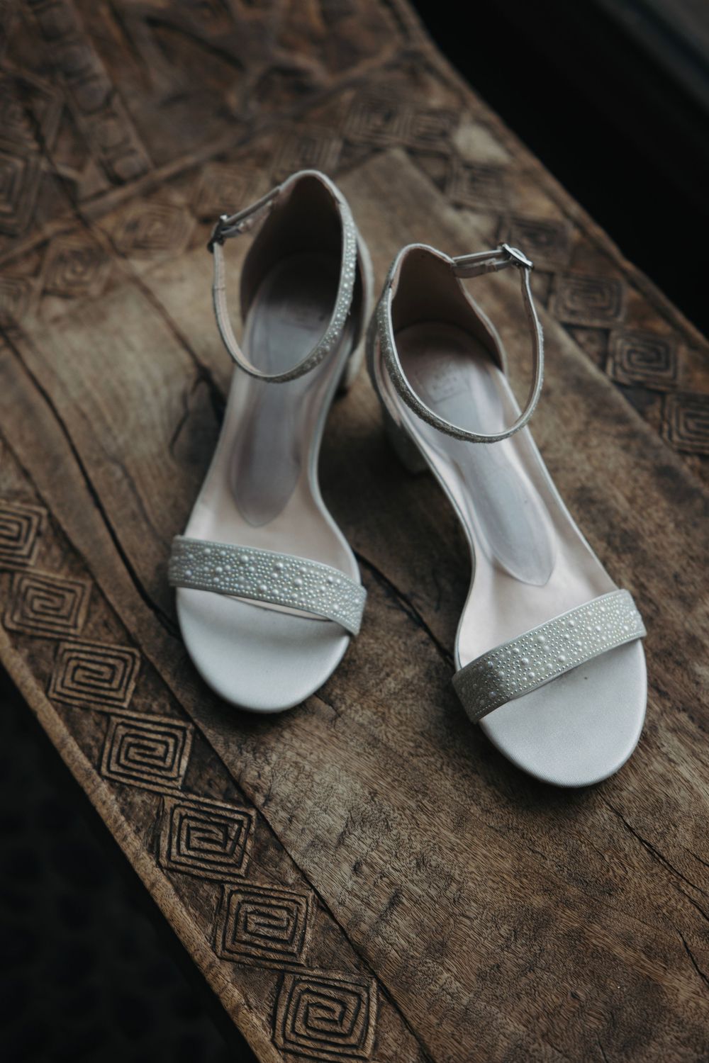 White bridal sandals with delicate beading displayed on rustic wooden surface.