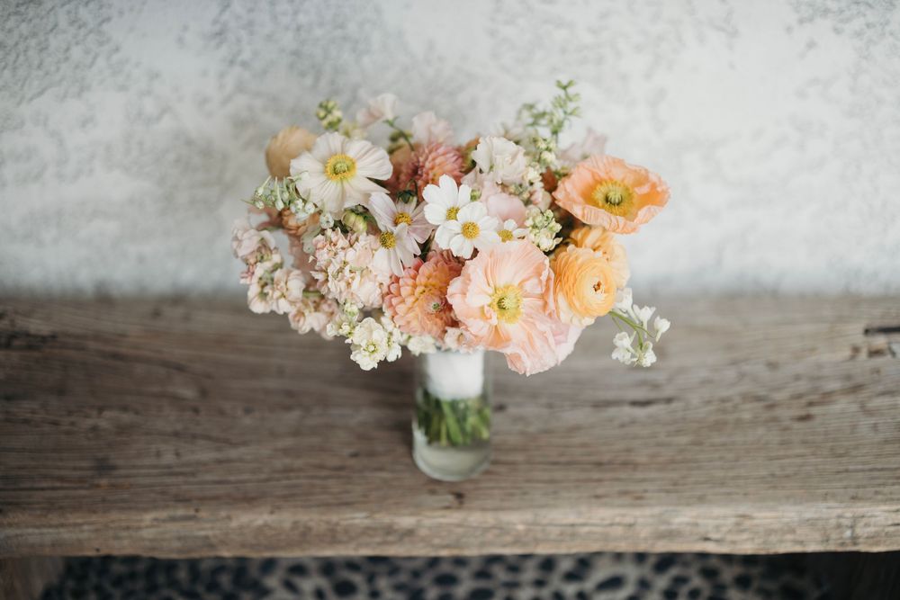 Soft pastel floral arrangements with peach and white blooms on rustic wood surface.